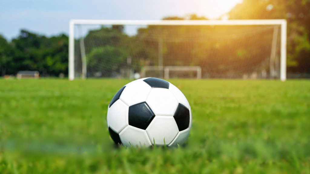 Un balón de fútbol en primer plano, al fondo la cancha